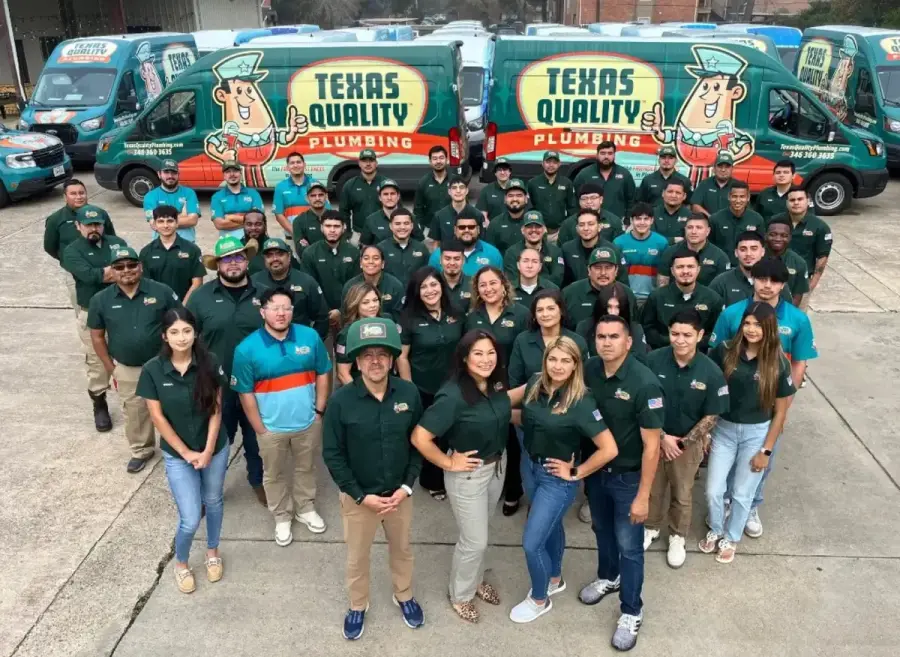 The full Texas Quality Plumbing team with the company's wrapped service vans